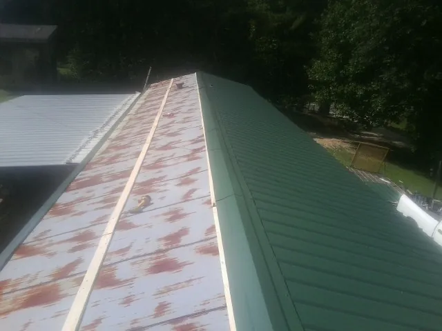 Old rusted panels beside newly installed green metal roofing — Wind Damage Roof Repair by Roofing Brothers in Barbourville