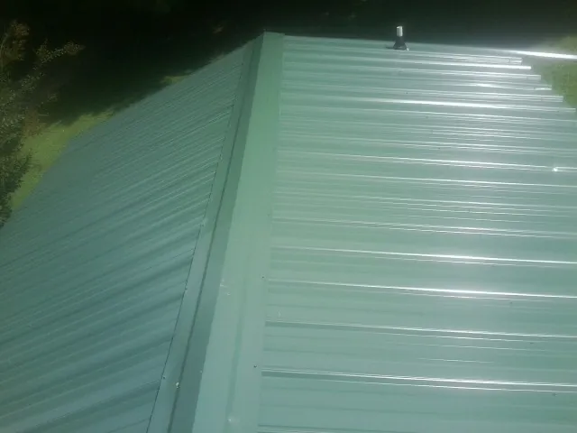New green metal panels meeting at the ridge of a roof — Flat Roof Repair work by our crew in Barbourville