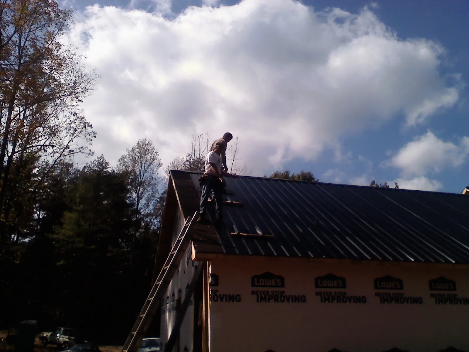 Roofer fastening dark metal panels high against a cloudy sky, from a Roof Inspection job in Barbourville