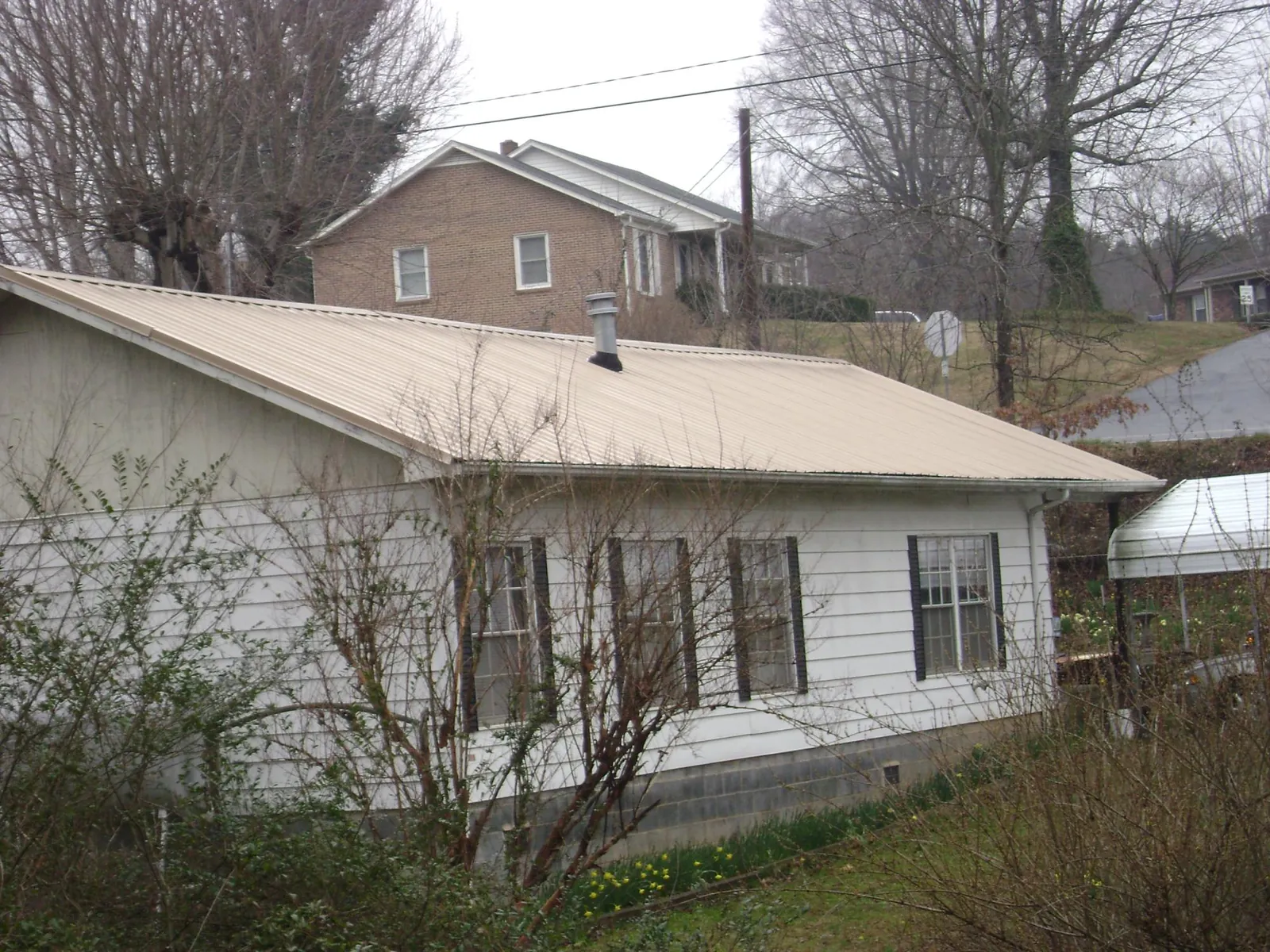Tan metal roof on a white sided house set into a hillside — Commercial Roofing by Roofing Brothers in Barbourville